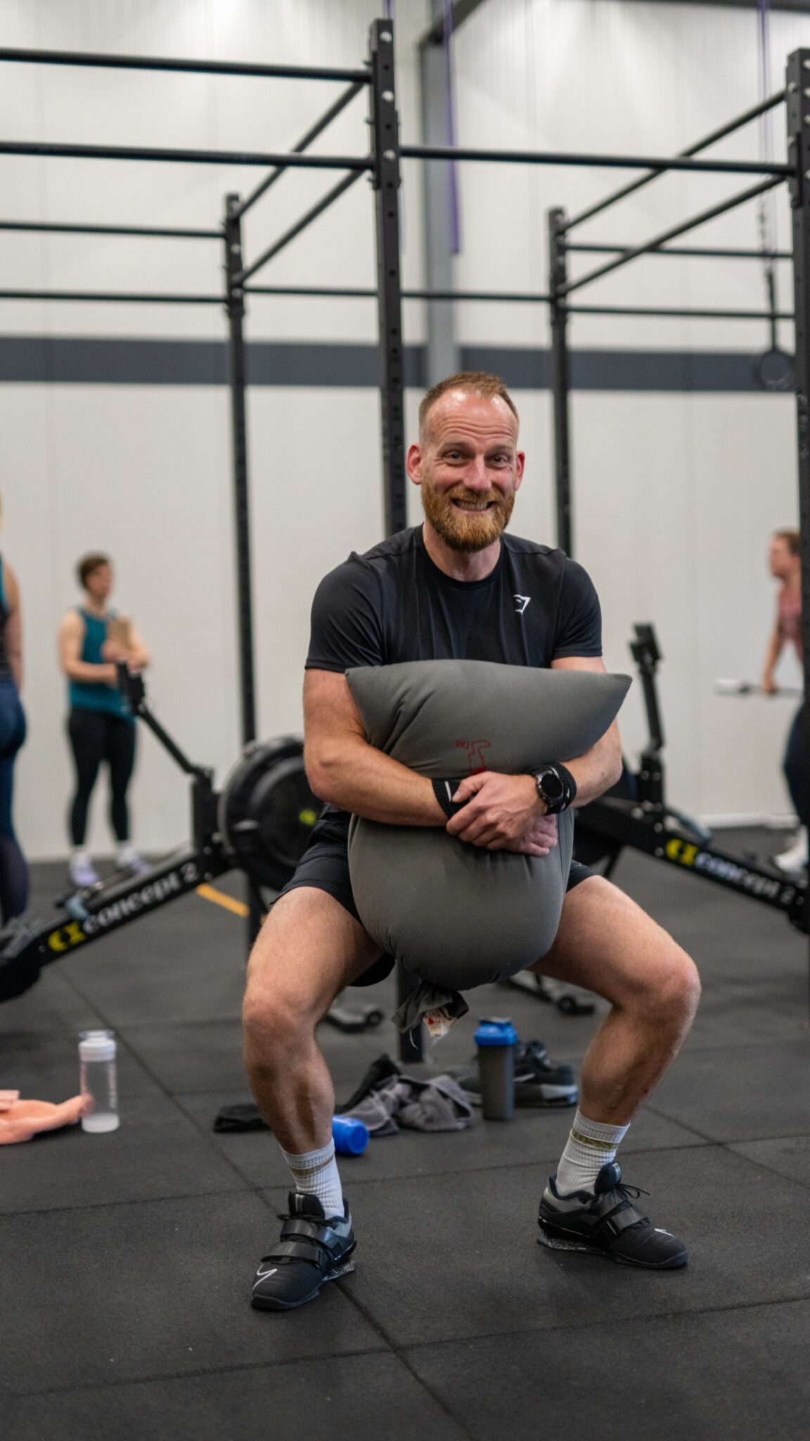 Lid maakt lachend een squat met een sandbag op de schouders